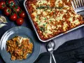 Herzhafter Kritharaki Auflauf mit Hackfleisch und Feta, garniert mit Thymian. Daneben frische Tomaten und Knoblauch.