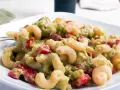 Ein cremiger nudelsalat mit avocado, Tomaten und Gewürzen auf einem weißen Teller.