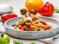 Ein köstlicher nudelsalat mit essig, garniert mit frischem Basilikum, Kirschtomaten und Mozzarella-Kugeln.