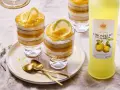 Erfrischendes Limoncello Tiramisu im Glas, geschichtet mit Biskuit und Zitronencreme, garniert mit Zitronenscheiben. Daneben eine Flasche Limoncello.
