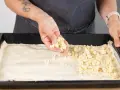 Hände verteilen Streusel auf einem Teigboden für ein Prasselkuchen Rezept DDR.