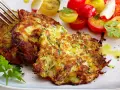 Goldbraune Zucchini-Puffer, knusprig gebraten, serviert mit einem bunten Tomatensalat und frischer Petersilie. Ein Genuss!