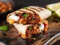 Zwei saftige Burritos, gefüllt mit Hackfleisch, Bohnen und einem Klecks Sauerrahm, sind ein köstliches burrito rezept. Garniert mit Koriander und Chili.