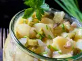 Ein köstlicher Kartoffelsalat ohne Mayo, mit Gurken, Zwiebeln und frischen Kräutern, serviert in einem Glas.