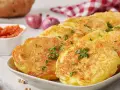Goldbraune Kartoffelpuffer, garniert mit Petersilie, sind ein köstliches Beispiel für Rezepte mit Kartoffeln als Hauptspeise. Dazu passen Tomatensoße und Zwiebeln.