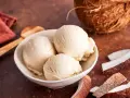 Schaufeln cremiges Kokoseis, perfekt zum Kokoseis selber machen mit Eismaschine. Daneben Kokosnussstücke.