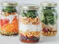 Drei Gläser mit geschichtetem Salat: Reis, Mais, Bohnen, Tomaten, Karotten und Spinat. Perfekt für unterwegs!