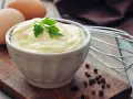Cremige Mayonnaise in einer Schüssel, garniert mit Petersilie. Eier und ein Schneebesen deuten auf ein hausgemachtes mayonnaise rezept hin.