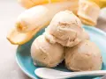 Cremiges Bananeneis, ganz einfach eis selber machen ohne eismaschine. Dazu reife Bananen und eine weiße Löffel auf blauem Teller.