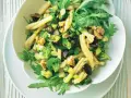 Frischer nudelsalat mit brokkoli, Walnüssen, Oliven und Rucola in einer weißen Schüssel.