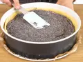 Ein Mohnkuchen mit Puddingfüllung wird in einer Springform vorbereitet. Eine Hand glättet die Mohnmasse mit einem Spatel.
