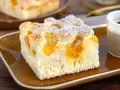 Saftiger Buttermilchkuchen mit Mandarinen, bestäubt mit Puderzucker, auf einem braunen Teller neben einer Tasse Kaffee.