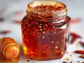 Glas mit würzigem Honig, ideal für ein Hot Honey Rezept. Daneben ein Honiglöffel mit flüssigem Honig.