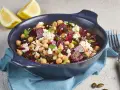 Ein bunter rote Bete Kichererbsen Salat mit Feta und Kürbiskernen in einer blauen Schüssel, garniert mit Petersilie und Zitronenspalten.