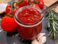 Frisches, selbstgemachtes Ketchup in einem Glas, umgeben von Tomaten, Knoblauch und Rosmarin. Perfekt zum Ketchup selber machen!