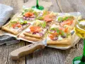 Flammkuchen mit Lachs und Crème fraîche, garniert mit Rucola und Dill, auf rustikalem Holztisch.
