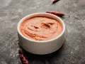 Eine Schale mit cremiger Piri Piri Sauce, umgeben von getrockneten Chilis auf dunklem Untergrund.