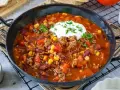 Herzhaftes Chili con Carne mit Hackfleisch, Kidneybohnen, Mais und Paprika, garniert mit einem Klecks Sauerrahm und Petersilie.