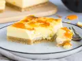 Ein Stück Mandarinen Schmand Kuchen Blech mit fruchtiger Glasur auf einem Teller, daneben ein Stück mit einer Gabel.