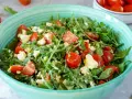 Frischer Rucolasalat mit saftigen Tomaten und cremigem Käse in einer türkisfarbenen Schüssel.