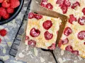 Schneller Kuchen mit gefrorenen Himbeeren, bestreut mit Puderzucker und Mandelblättchen. Ein Genuss für jeden Anlass!