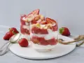 Zwei Gläser mit einem sommerlichen Dessert aus Erdbeeren und Sahne, garniert mit frischen Erdbeeren und Keksen. Ein schnell und einfach zubereitetes Genusserlebnis.