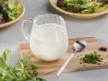 Ein Krug mit cremigem Ranch Dressing, daneben Schnittlauch und Petersilie. Perfekt für einen frischen Salat.