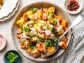 Kartoffelsalat mal anders: knusprige Kartoffelspalten mit cremiger Sauce, Frühlingszwiebeln und roten Zwiebelringen in einer rustikalen Schüssel.