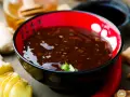 Schwarze Schüssel mit glänzender Teriyaki-Sauce, umgeben von Ingwer, Knoblauch und Chili. Ein köstliches teriyaki sauce rezept zum Nachkochen.