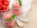 Erfrischendes Meloneneis selber machen: Rosa Sorbet in Gläsern mit Minze, daneben eine Schale mit Wassermelonenwürfeln.