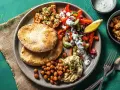 Ein bunter griechischer Salat mit Hummus, gerösteten Kichererbsen und Pitabrot. Dazu gewürfelter Tofu und ein Zitronenschnitz.