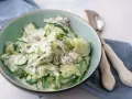 Frischer gurkensalat mit saurer sahne, garniert mit Dill und roten Zwiebeln, serviert in einer hellgrünen Schüssel.