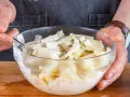 Hände mischen in einer Glasschüssel den cremigen selleriesalat nach Omas Rezept.