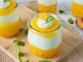 Erfrischendes Solero Dessert im Glas mit Mango-Fruchtsoße, weißer Creme und einem Klecks Sahne, garniert mit Minze und Orangenspalte.