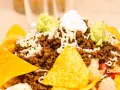 Schichtsalat mit Hackfleisch, Käse, Guacamole und saurer Sahne, garniert mit knusprigen Nachos.