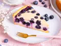 Ein Stück Blaubeerkuchen auf einem Teller, inspiriert von Landfrauen Kuchen Rezepten. Mit frischen Blaubeeren und zarter Füllung.