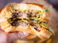 Ein saftiger Burger mit zwei Rindfleisch-Patties, Salat und der unverwechselbaren Big Mac Sauce, gehalten in einer Hand.
