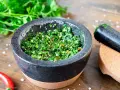 Frisches Chimichurri-Rezept im Mörser, bereit zum Verfeinern von Grillgut. Kräuter, Chili und Gewürze sind fein gehackt.