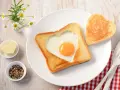 Herzförmiger Toast mit Ei, daneben ein Herzbutterstück und ein Herz-Toast. Ein liebevolles Frühstück.
