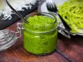 Frisches Rucola Pesto in einem Glas mit Löffel, daneben Pasta.