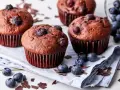 Saftige schoko blaubeer muffins, garniert mit frischen Blaubeeren und Schokostückchen, liegen auf einem Leinentuch.