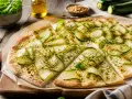 Flammkuchen mit Zucchini, belegt mit dünnen Zucchinischeiben und Kräutern, auf einem Holzbrett.