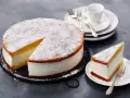 Eine köstliche Quark Sahne Torte, bestäubt mit Puderzucker, wartet darauf, genossen zu werden. Ein Stück ist bereits auf einem Teller angerichtet.