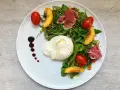 Salat mit Nektarinen, Burrata, Prosciutto und Kirschtomaten, garniert mit Balsamico-Dressing.