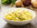 Omas Kartoffelsalat Rezept Original: Ein cremiger Kartoffelsalat mit Zwiebeln und Schnittlauch in einer weißen Schüssel, bereit zum Genießen.