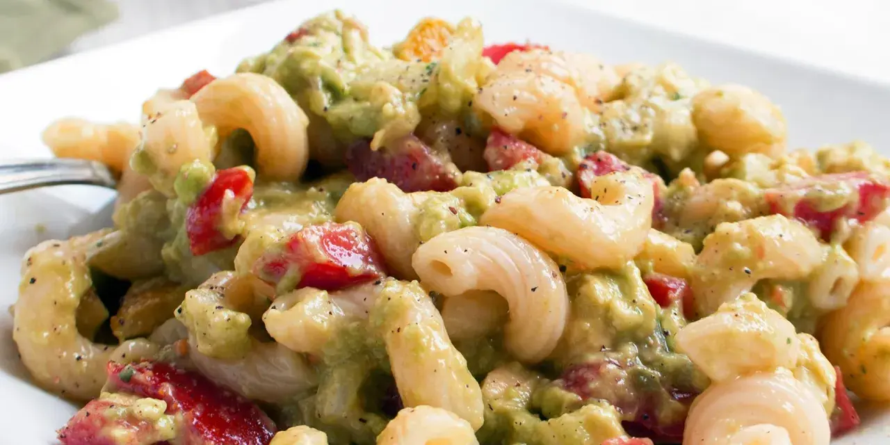 Ein cremiger nudelsalat mit avocado, Tomaten und Gewürzen auf einem weißen Teller.