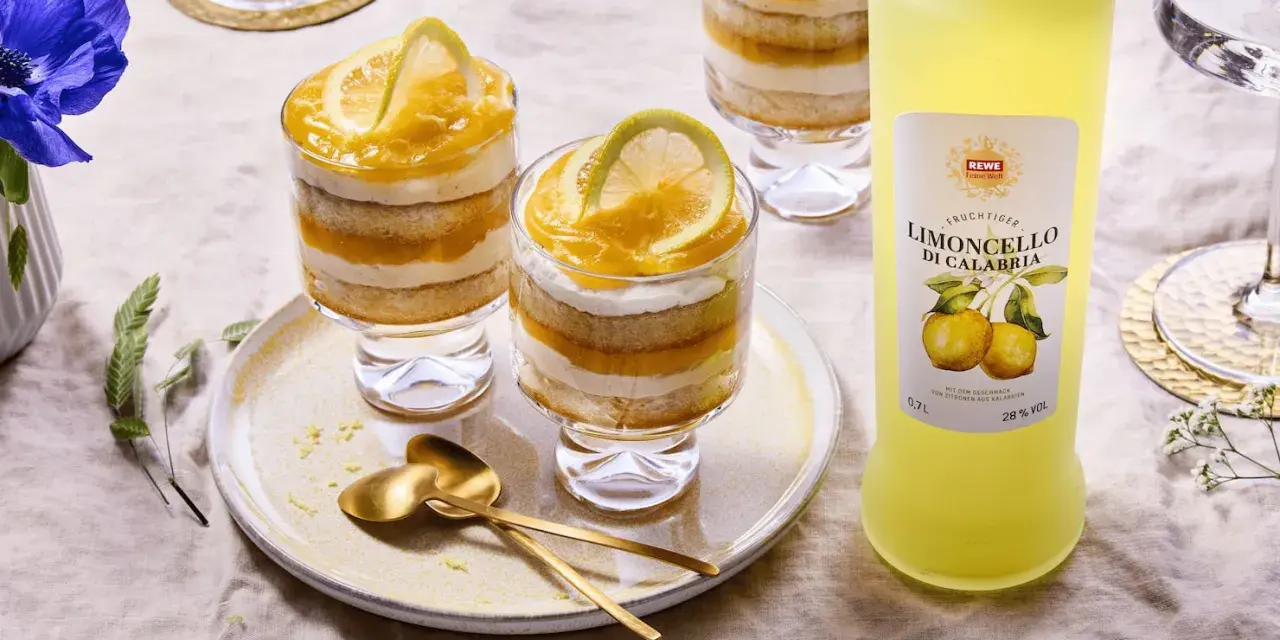 Erfrischendes Limoncello Tiramisu im Glas, geschichtet mit Biskuit und Zitronencreme, garniert mit Zitronenscheiben. Daneben eine Flasche Limoncello.