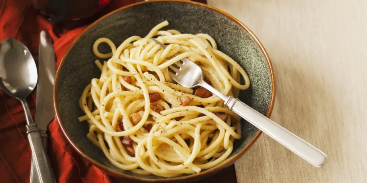Eine Schüssel Spaghetti mit Speck und Pfeffer, eine köstliche Carbonara ohne Ei, serviert mit einem Glas Rotwein.
