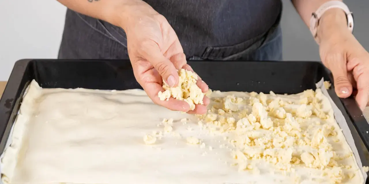 Hände verteilen Streusel auf einem Teigboden für ein Prasselkuchen Rezept DDR.