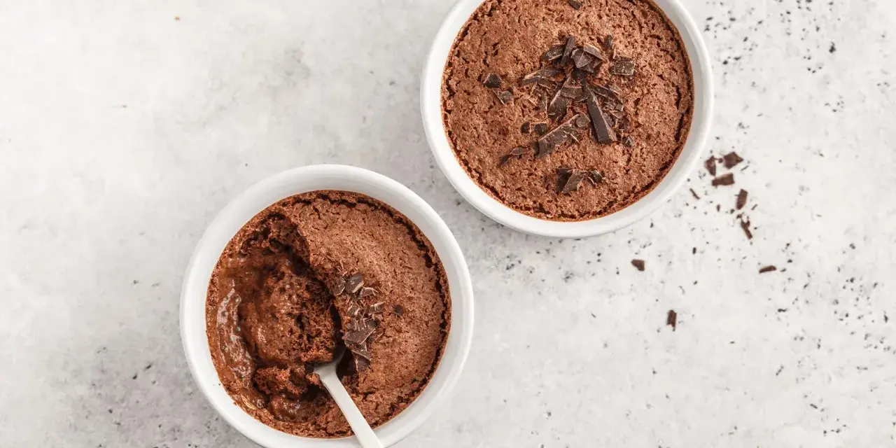 Zwei Schokoladenmousse-Portionen, garniert mit Schokostückchen. Ein Löffel steckt in einer der Schalen, bereit für ein schnelles Dessert.